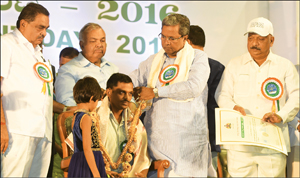 Chief Minister Siddharamaiah is seen presenting the ‘Environment Award’ to Dr. Chandra, Ayurveda Doctor from T. Narasipur taluk in Mysuru district. Others seen are Ministers Ramanath Rai, Ramalinga Reddy and Roshan Baig. 