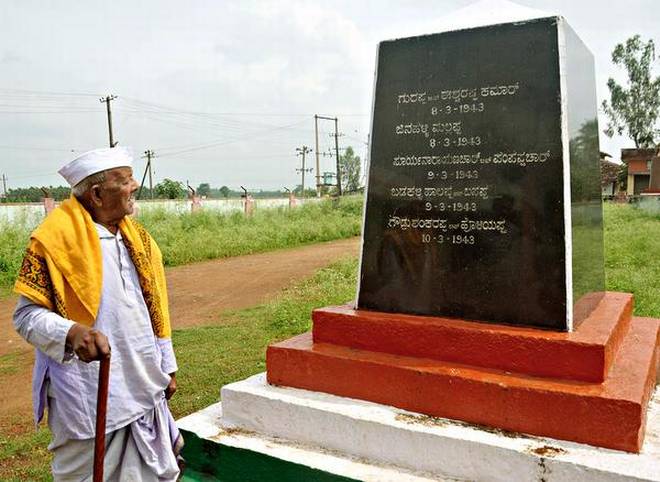 Freedom fighter N.S. Huchrayappa near the pillar erected on the outskirts of Esur with the names of freedom fighters who were hanged engraved on it. | Photo Credit: VAIDYA;VAIDYA - VAIDYA